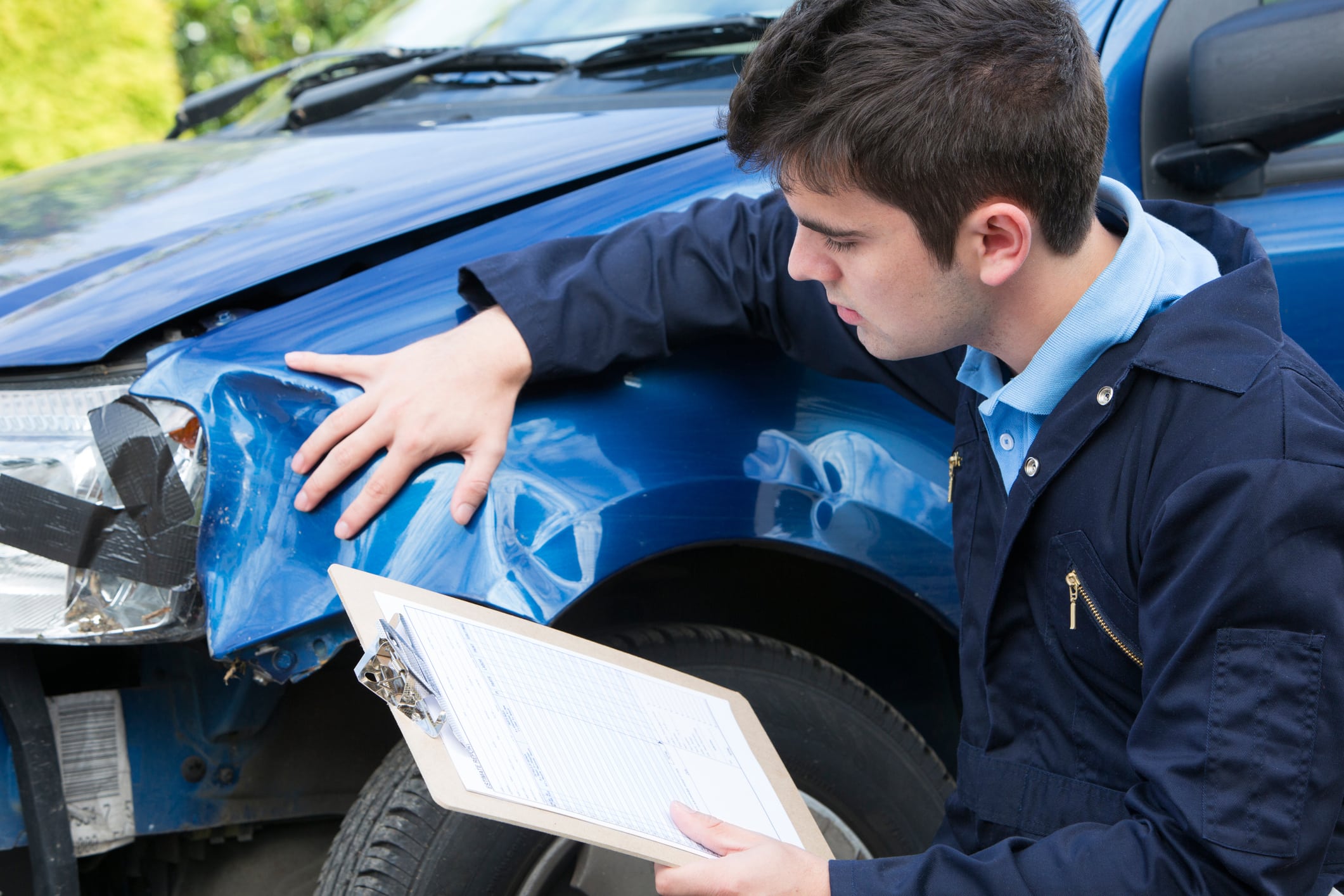 A repair man inspecting damage to a rental car.